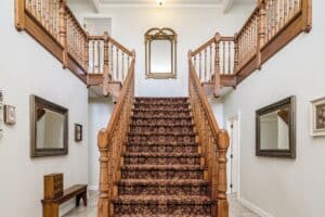 Big wooden staircase with a vintage carpet inside an apartment with white walls